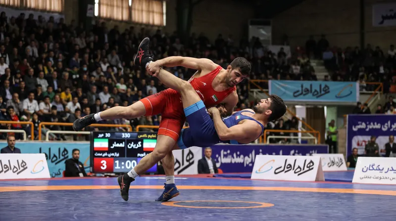A freestyle wrestler executing a low double leg takedown on a wrestling mat.