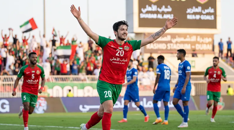 A football player in a red and green jersey walking off the pitch looking frustrated.