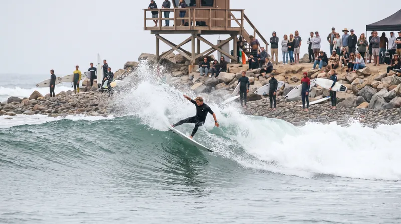 A male surfer performs a high aerial maneuver over a wave during the Trestles Pro competition.