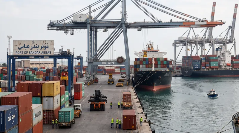 A massive container ship being loaded with colorful shipping containers at a busy commercial port.