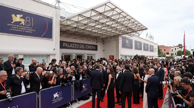 Red carpet scene at the Venice Film Festival with photographers and guests in formal attire.