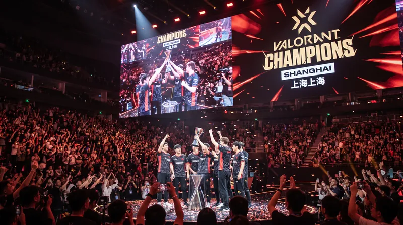 A massive esports stage with bright lights and large screens displaying the Valorant Champions logo in an arena.