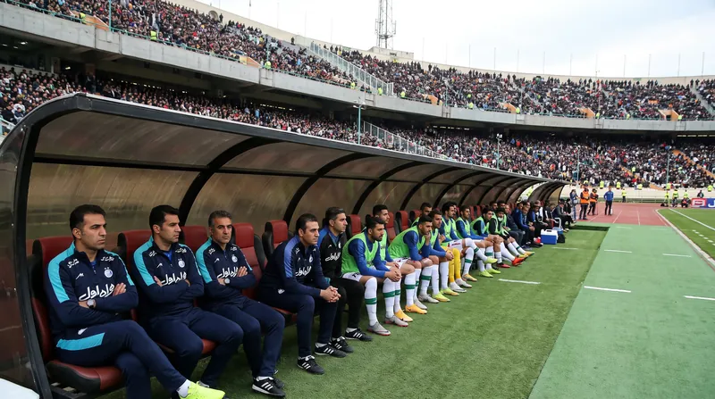An empty soccer team bench in a modern stadium under bright sunlight.