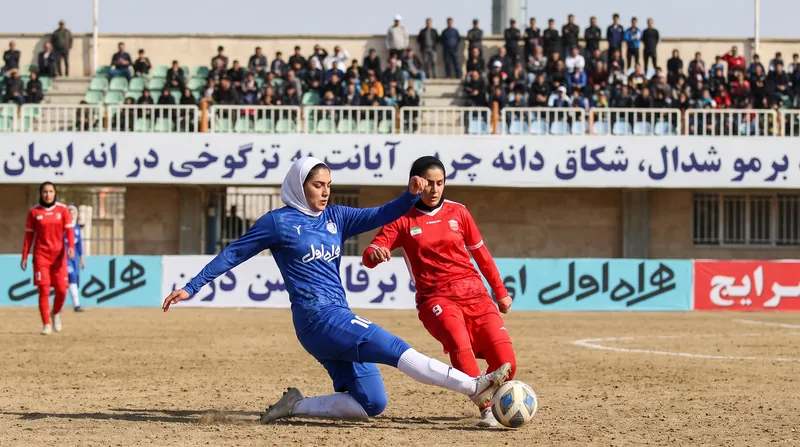 نمایی از بازی فوتبال زنان در ایران با حضور بازیکنان با پوشش ورزشی در زمین چمن