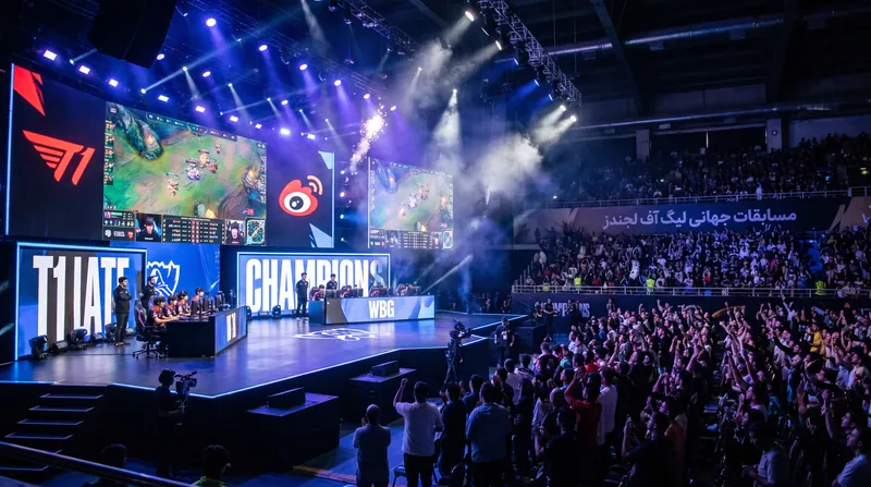 A massive esports arena filled with fans, featuring large screens showing League of Legends gameplay on stage.