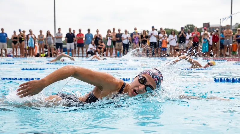 A female swimmer emerging from the ocean water wearing a swim cap and goggles.
