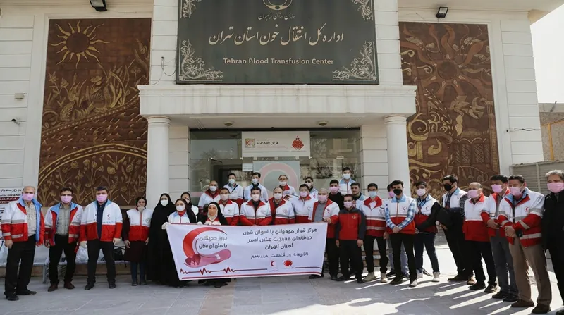 پزشکان داوطلب با روپوش سفید و نیروهای هلال‌احمر با جلیقه قرمز در حال معاینه کودکان در یک مدرسه روستایی